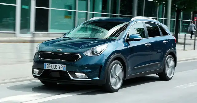 Ciemnoniebieski Kia Niro jedzie ulicą obok nowoczesnego budynku.