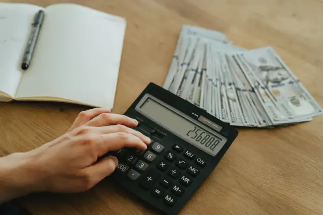 Ręka wpisuje kwotę na kalkulatorze obok stosu banknotów. Planowanie finansowe, jak zatrzymać odsetki u komornika, wymaga precyzji.