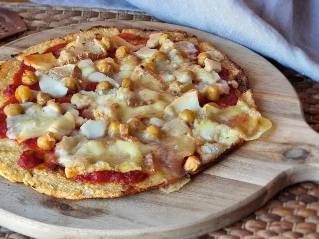 Pizza sin queso con garbanzos y trozos de queso derretido sobre una base crujiente.