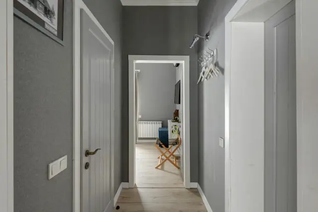 Pasillos con encanto, con paredes grises, puertas blancas y un cuadro en la pared. Se vislumbra una habitación con un radiador y un banco.