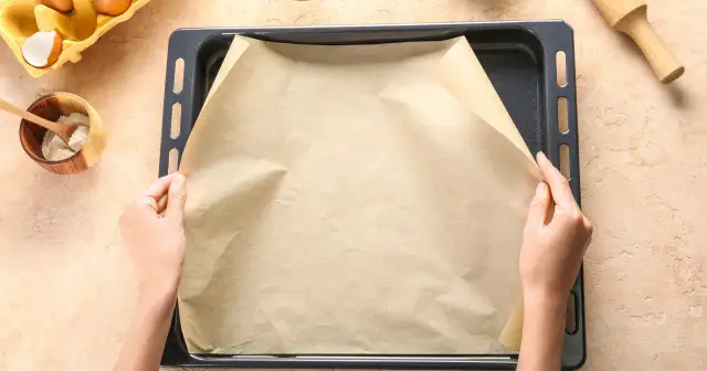 Dłonie rozkładają papier do pieczenia na blasze. To świetne rozwiązanie, co zamiast papieru do pieczenia, gdy chcesz uniknąć przypalenia.