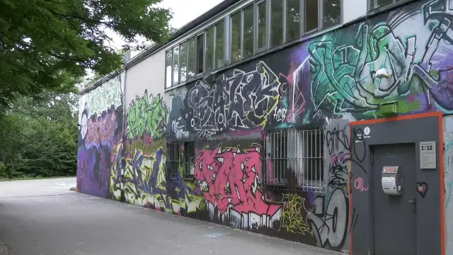Bunte Graffiti-Kunst bedeckt die Wand eines Gebäudes, mit Fenstern und einer Tür.