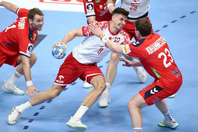Gracz w białej koszulce z numerem 9 próbuje rzucić piłkę, podczas gdy obrońca w czerwonej koszulce z numerem 23 stara się mu przeszkodzić. Emocjonująca akcja w meczu piłki ręcznej.