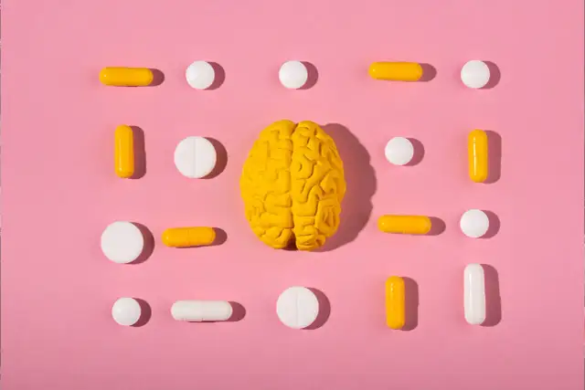 Żółty model mózgu otoczony białymi i żółtymi tabletkami i kapsułkami. Czy to symbol wsparcia dla serotoniny?