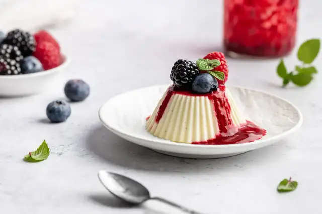 Vegane Panna Cotta mit Beerensoße und frischen Beeren, ein leichter Genuss.