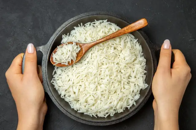 Sypki ryż basmati w misce, nabierany drewnianą łyżką, trzymany przez dwie dłonie.