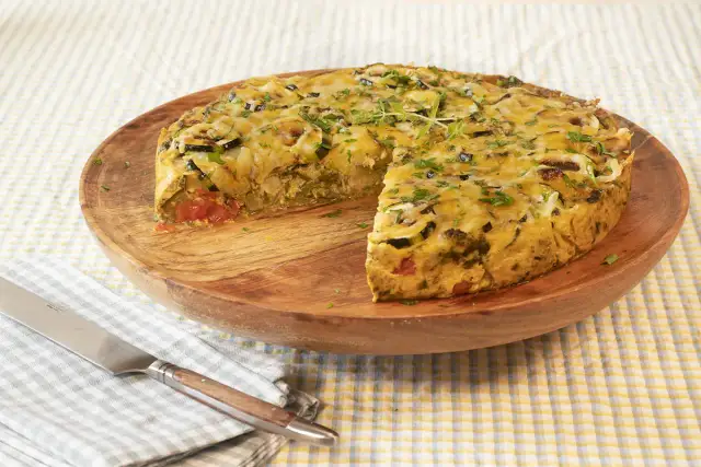 Pastel de acelgas con verduras y queso gratinado, servido en plato de madera.