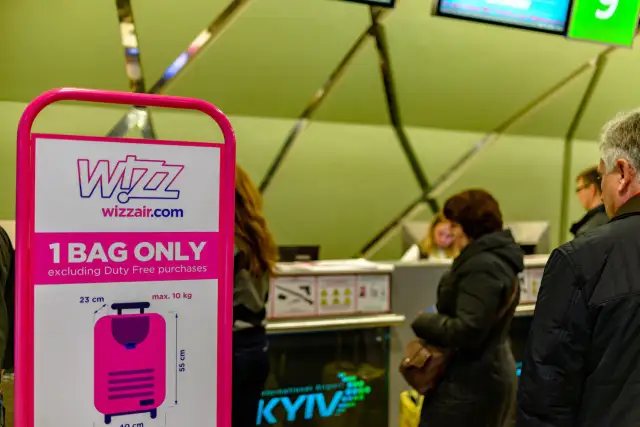 Tablica Wizz Air z informacją o limicie bagażu podręcznego i ludzie w tle.