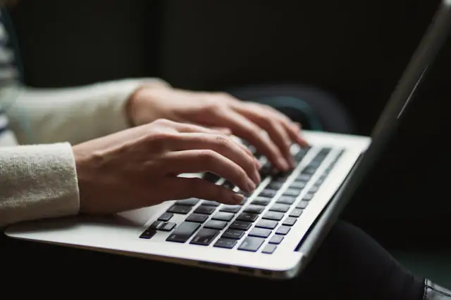 Dłonie piszą na laptopie. Ktoś przygotowuje wypowiedzenie umowy o pracę po angielsku, szukając wzoru.