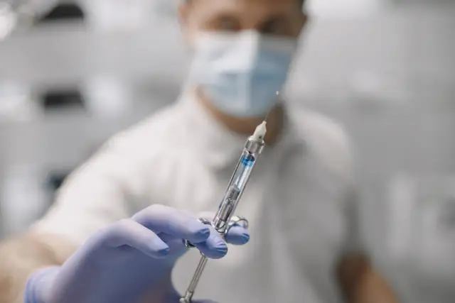 Dłoń w niebieskiej rękawiczce trzyma strzykawkę dentystyczną z igłą.