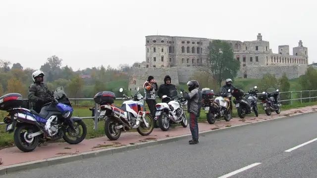Motocykliści i ich maszyny na tle ruin zamku w pochmurny dzień.