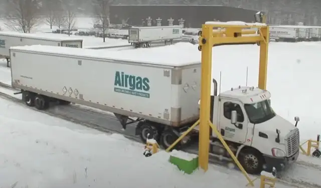 Ciężarówka z naczepą Airgas pod żółtą bramownicą w śnieżny dzień.