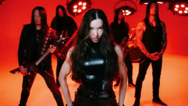 Wokalistka zespołu Arch Enemy w czarnym, błyszczącym stroju, z gitarzystami w tle, na tle czerwonych świateł.