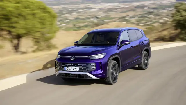 Fioletowy VW Tayron jedzie po krętej drodze wśród wzgórz.