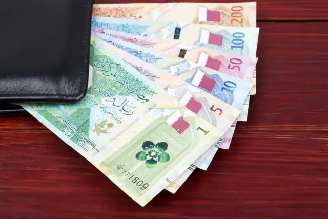 Katar jaka waluta? Na zdjęciu widać stos banknotów katarskich riali, od 1 do 200, częściowo schowanych w czarnym portfelu.