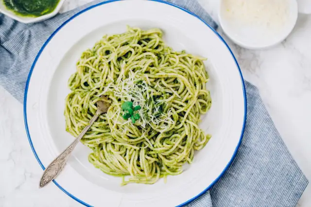 Porcja spaghetti z zielonym pesto, posypana parmezanem, na białym talerzu.
