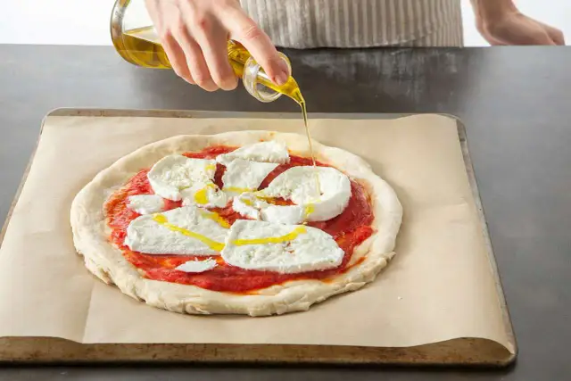 Oliwa z oliwek spływa na pizzę z mozzarellą i sosem pomidorowym, przygotowywaną w Thermomixie.