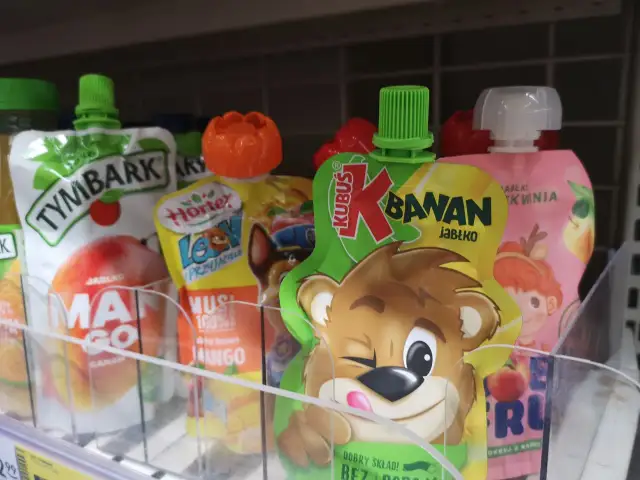 Czy musy owocowe są zdrowe dla dorosłych? Na półce widać różne musy owocowe, m.in. Kubuś banan jabłko, Tymbark, Hortex.