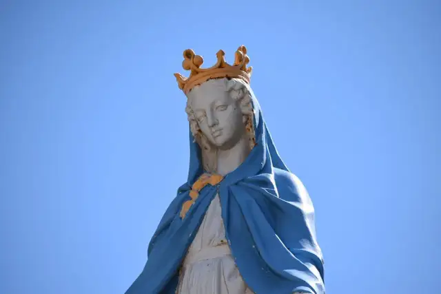 Posąg Matki Boskiej w koronie na tle błękitnego nieba.