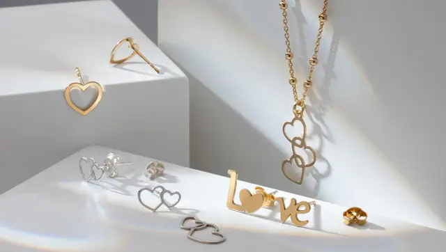Złota biżuteria w kształcie serc i napis "love" na białym tle.