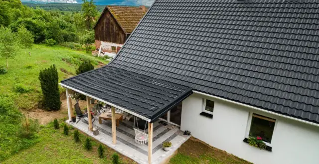 Nowy, czarny dach z blachodachówki nad tarasem i domem. Wymiana dachu zakończona sukcesem, dom zyskał nowy, nowoczesny wygląd.