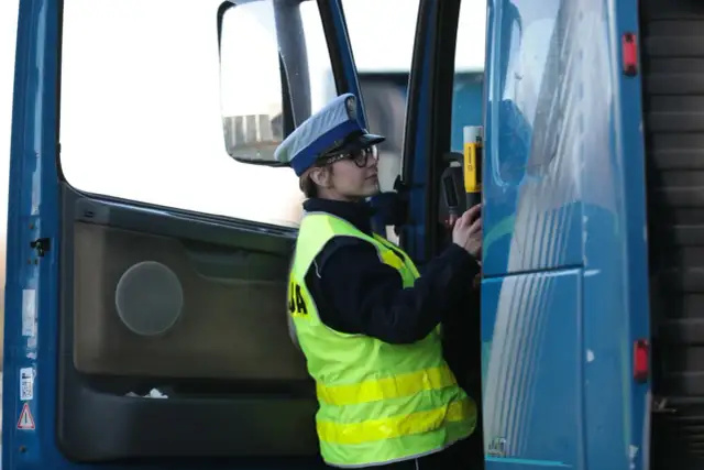 Policjantka w kamizelce odblaskowej i czapce przykłada alkomat do drzwi ciężarówki.