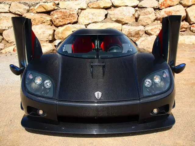 Czarny Pagani z otwartymi drzwiami, wykonany z włókna węglowego, z czerwonymi siedzeniami, na tle kamiennej ściany.