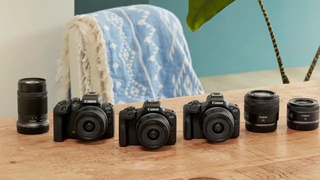 Trzy czarne aparaty Canon EOS z obiektywami i dodatkowe obiektywy na drewnianym stole.