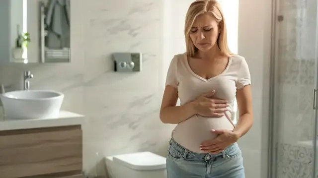 Kobieta w ciąży trzyma się za brzuch, zmartwiona. Czy to wzdęcia, czy skurcze w ciąży?