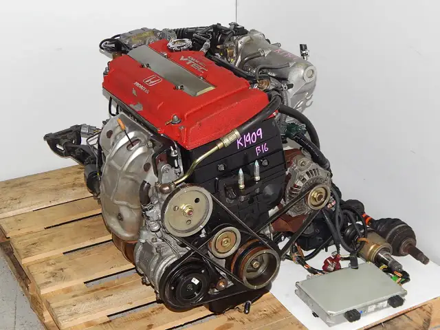 Silnik Honda VTEC z czerwonymi pokrywami zaworów, na drewnianej palecie.