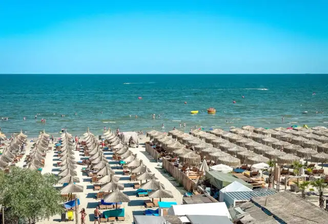 Słoneczne rumuńskie wakacje nad Morzem Czarnym. Plaża pełna leżaków i parasoli, ludzie kąpią się i relaksują.