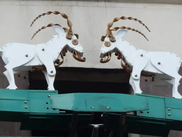 Dwie białe, metalowe kozy z kręconymi rogami patrzą na siebie.