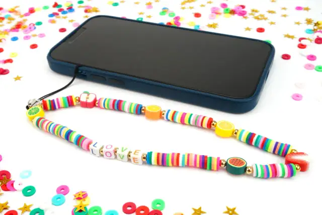 Comment faire un bracelet de téléphone : un cordon coloré avec des perles fruits et lettres "LOVE" est attaché à un smartphone.