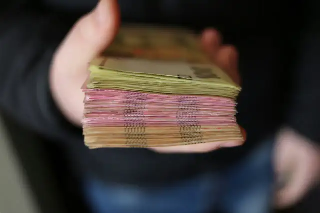 Gruba paczka banknotów, różowych i żółtych, trzymana w dłoni. To zabezpieczenie finansowe, które daje poczucie bezpieczeństwa.