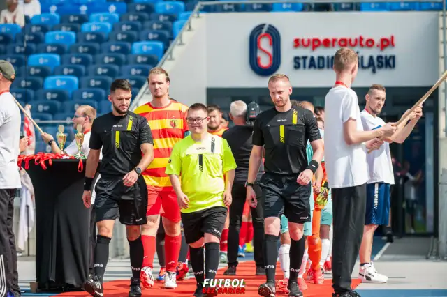 Piłkarze i sędziowie wchodzą na murawę stadionu.