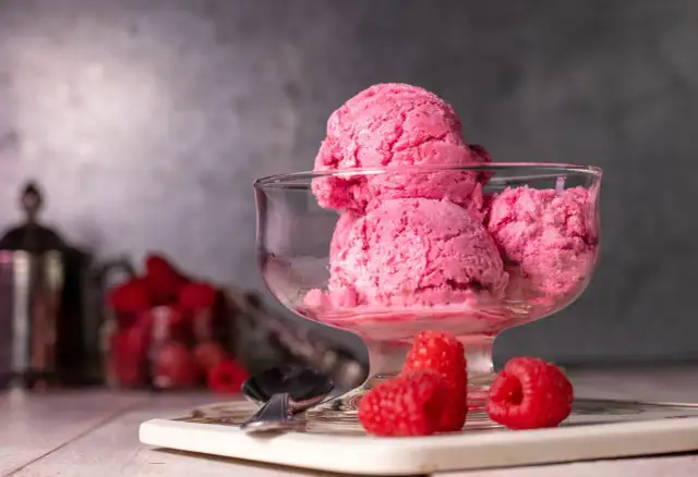 Ein Glas mit cremigem, veganem Himbeereis, garniert mit frischen Himbeeren. Perfekt für einen heißen Sommertag.