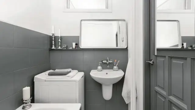 Baño moderno con azulejos grises, lavadora y lavabo. Un ejemplo de reformas de baños antes y después, con un estilo minimalista y funcional.