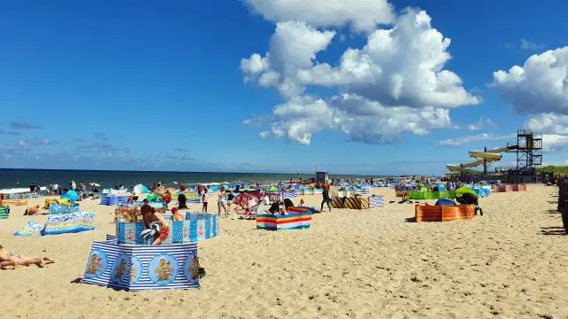 Władysławowo z dzieckiem: plaża pełna kolorowych parawanów, ludzi odpoczywających i bawiących się na piasku, w tle morze i zjeżdżalnie wodne.