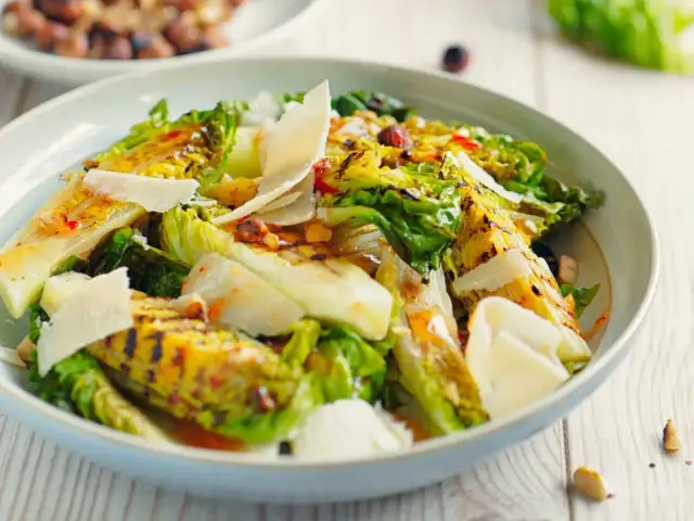 Deliciosa ensalada de cogollos a la parrilla, cubierta con lascas de queso parmesano y un aderezo vibrante.