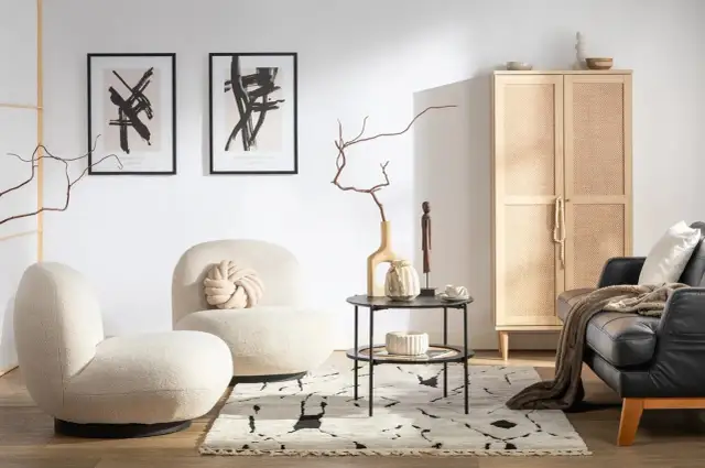 Przytulny salon w stylu hygge wnętrza. Jasne fotele, czarna skórzana kanapa, drewniana szafka z rattanowymi drzwiczkami i abstrakcyjne obrazy tworzą ciepłą atmosferę.
