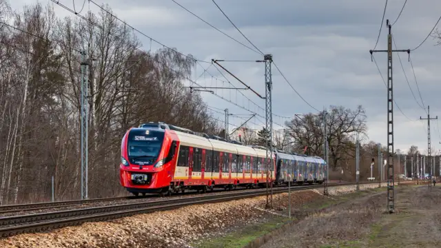 Czerwono-biały pociąg SKM S2 Chopin Airport jedzie po torach. System monitoringu ruchu pociągów śledzi jego trasę.