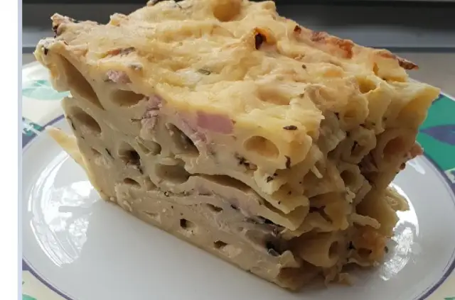 Kawałek zapiekanki makaronowej z serem i szynką na talerzu.