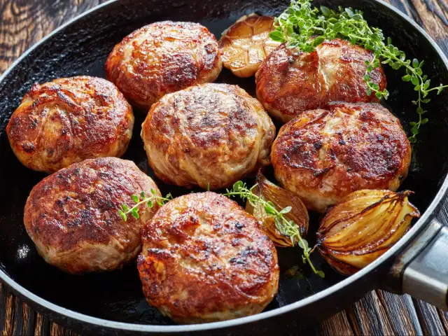 Usmażone kotlety na burgera z cebulą i ziołami na patelni.