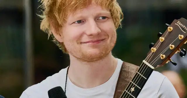 Ed Sheeran z gitarą, uśmiechnięty, w białej koszulce.