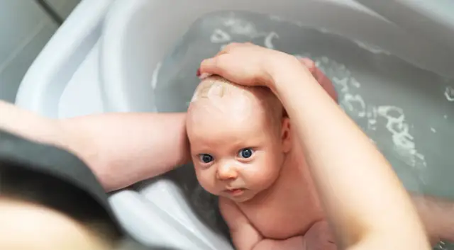 Niemowlę w wanience, myte przez rodzica. Czy można kąpać dziecko jak ma gorączkę? Woda może pomóc obniżyć temperaturę.