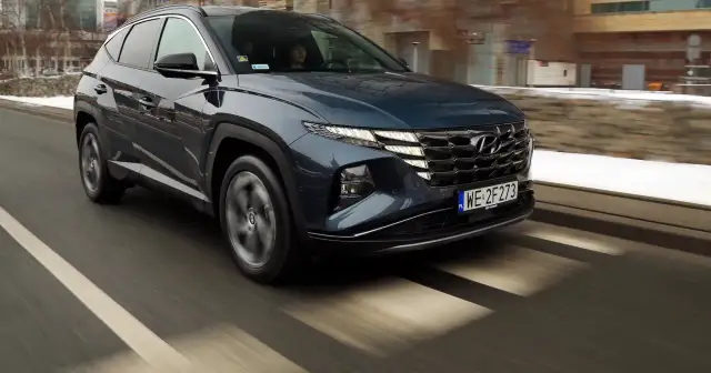 Ciemnogranatowy Hyundai Tucson jedzie po ulicy, widać jego przednią część i grill.