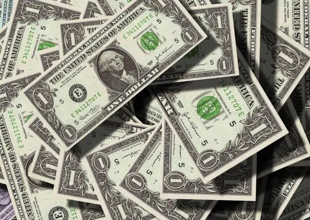 Stosy dolarowych banknotów. Kto ponosi koszty działu spadku u notariusza? Pieniądze mogą pomóc w tej kwestii.