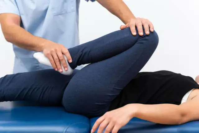 Fizjoterapeuta wykonuje ćwiczenia z pacjentem, którego noga jest zgięta w kolanie. To część terapii, która może pomóc w leczeniu zespołu sudeckiego.