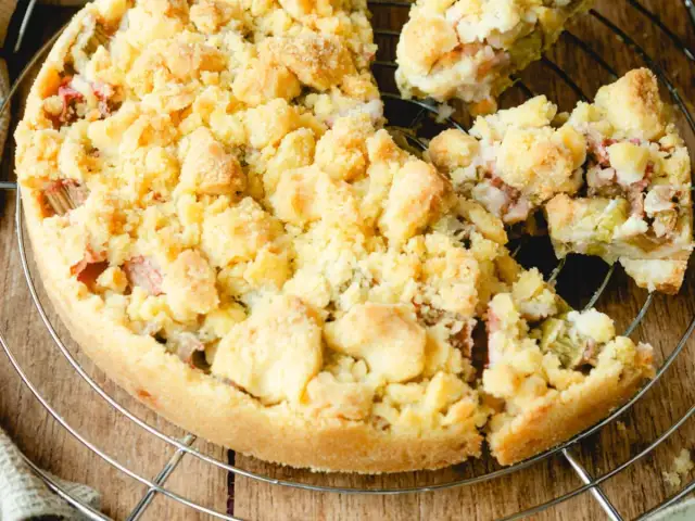 Ein köstlicher Rhabarberkuchen mit Streuseln, der auf einem Gitter abkühlt. Die süßen Streusel bedecken die saftige Rhabarberfüllung.