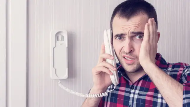 Zmartwiony mężczyzna dzwoni z telefonu domofonowego. Gdzie zgłosić niedziałający domofon?